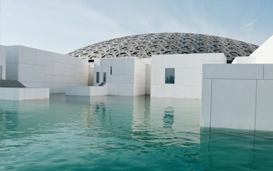 Louvre Abu Dhabi exterior with water reflection and dome.
