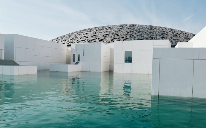 Louvre Abu Dhabi exterior with water reflection and dome.