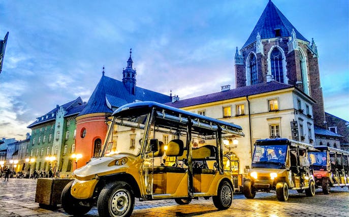 Golf carts in Krakow's Kazimierz Quarter near historic buildings at dusk.