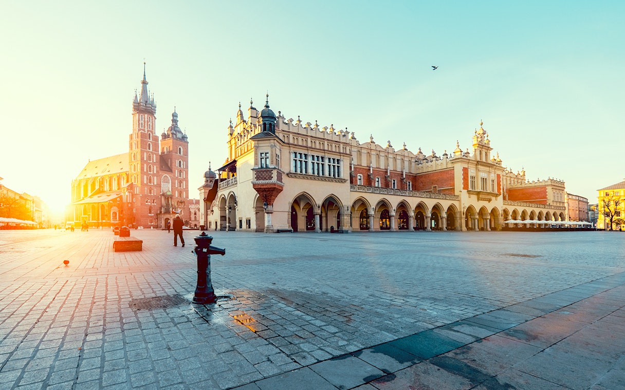 Krakow's Main Square with St. Mary's Basilica and Cloth Hall at sunrise.