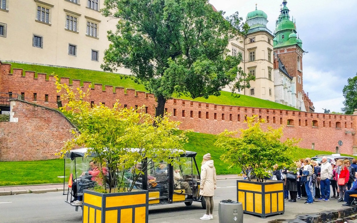 Golf cart tour near Wawel Castle, Krakow, with tourists and historic architecture.