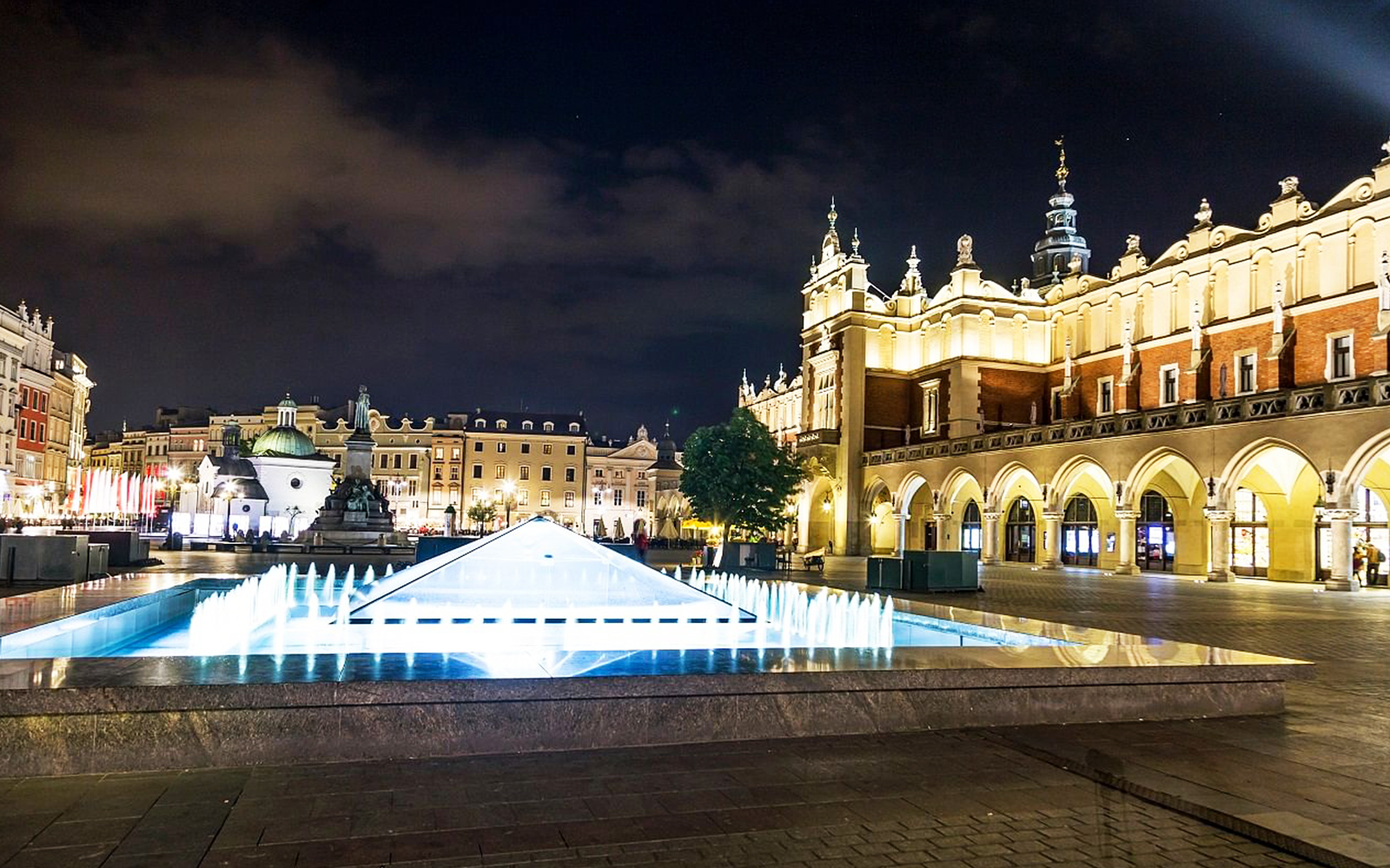 Krakow's Main Square at night with illuminated Cloth Hall and fountain.