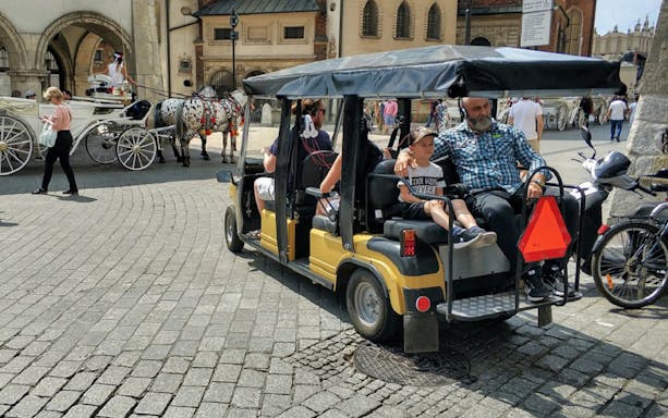 Golf cart tour in Krakow's Old Town near horse-drawn carriages.
