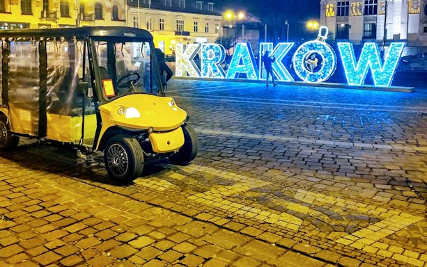 Golf cart in Krakow's Old Town with illuminated sign in background.