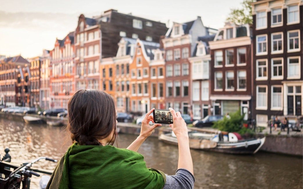 Person photographing Amsterdam canal houses during self-guided audio tour.