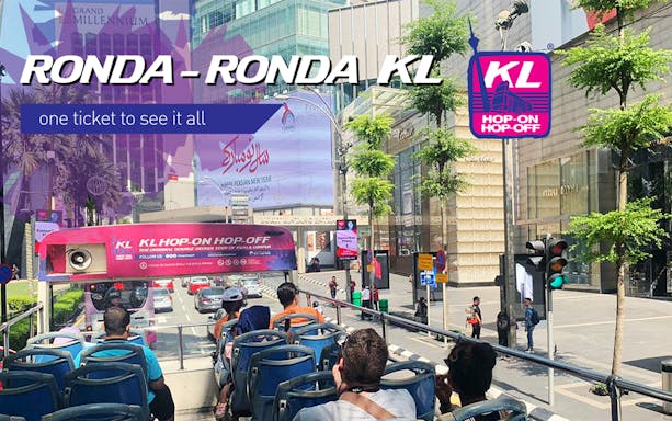 Open-top bus tour in Kuala Lumpur city center with passengers enjoying street views.