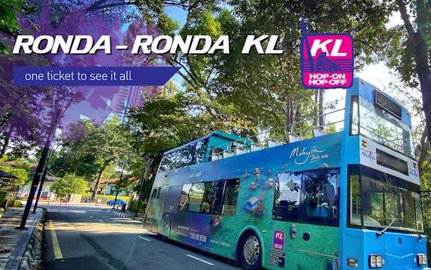 Double-decker tour bus on a tree-lined street in Kuala Lumpur, Malaysia.
