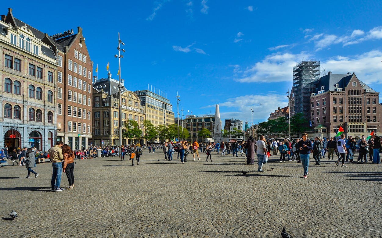 Dam Square with people walking and historic buildings, Amsterdam audio tour.