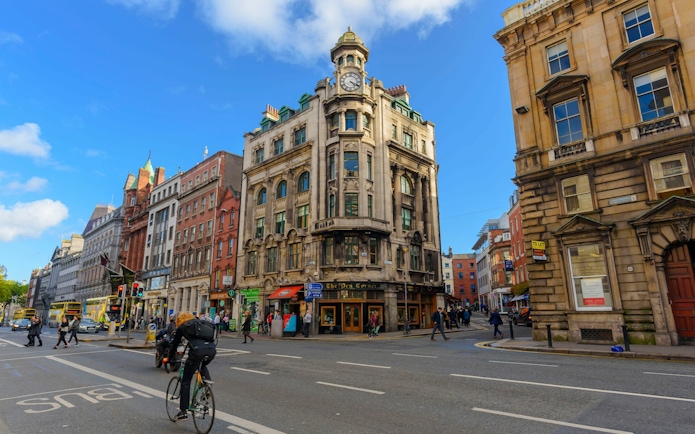 Historic building at a busy intersection in Dublin, featuring cyclists and pedestrians.