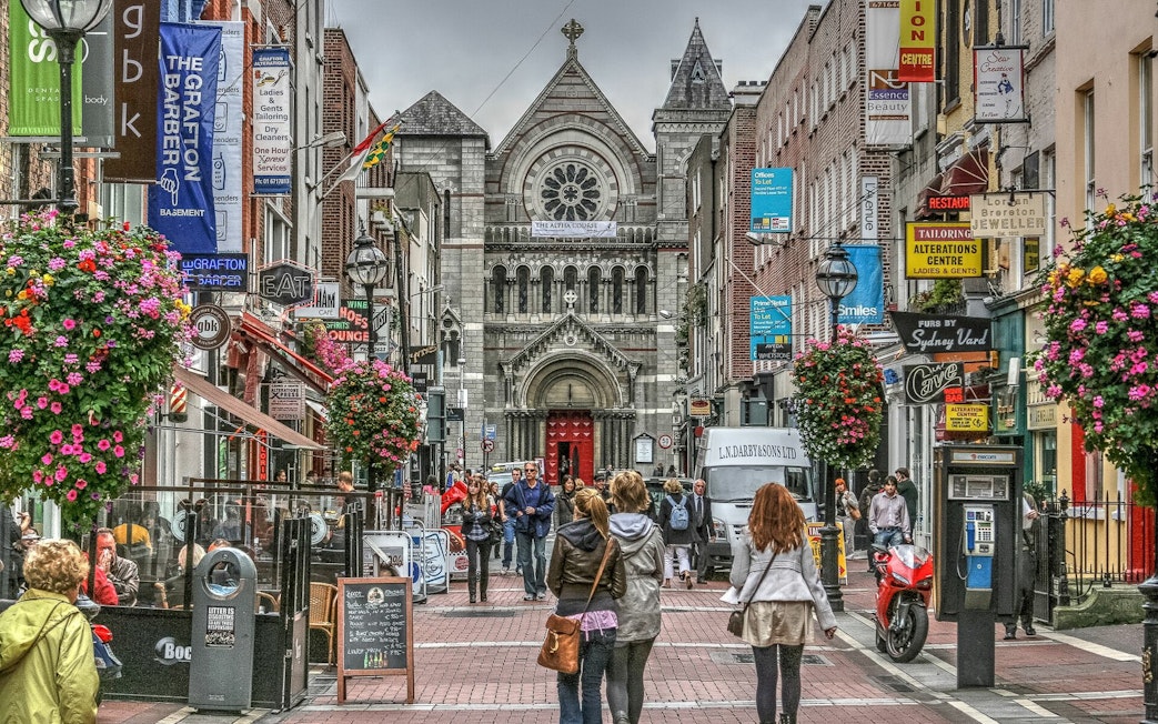 Pedestrians on a bustling street in Dublin with a historic church in the background.