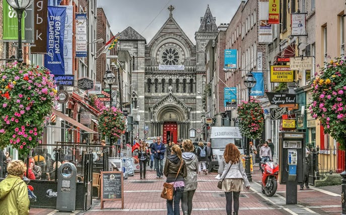 Pedestrians on a bustling street in Dublin with a historic church in the background.