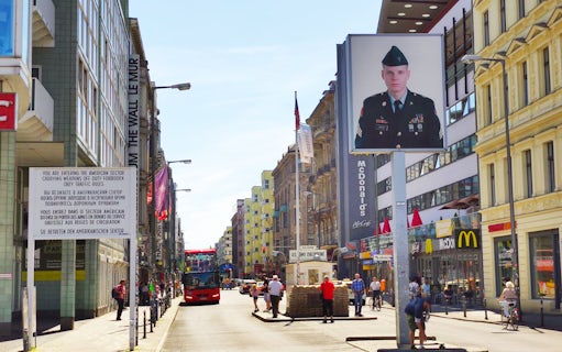 Berlin street view with Checkpoint Charlie, tour bus, and historical signage.