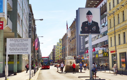 Berlin street view with Checkpoint Charlie, tour bus, and historical signage.