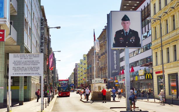 Berlin street view with Checkpoint Charlie, tour bus, and historical signage.