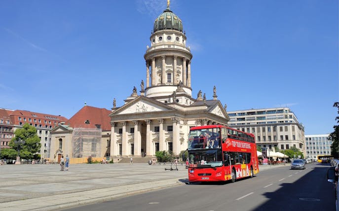 Red double-decker bus in front of Berlin's French Cathedral on a hop-on hop-off tour.