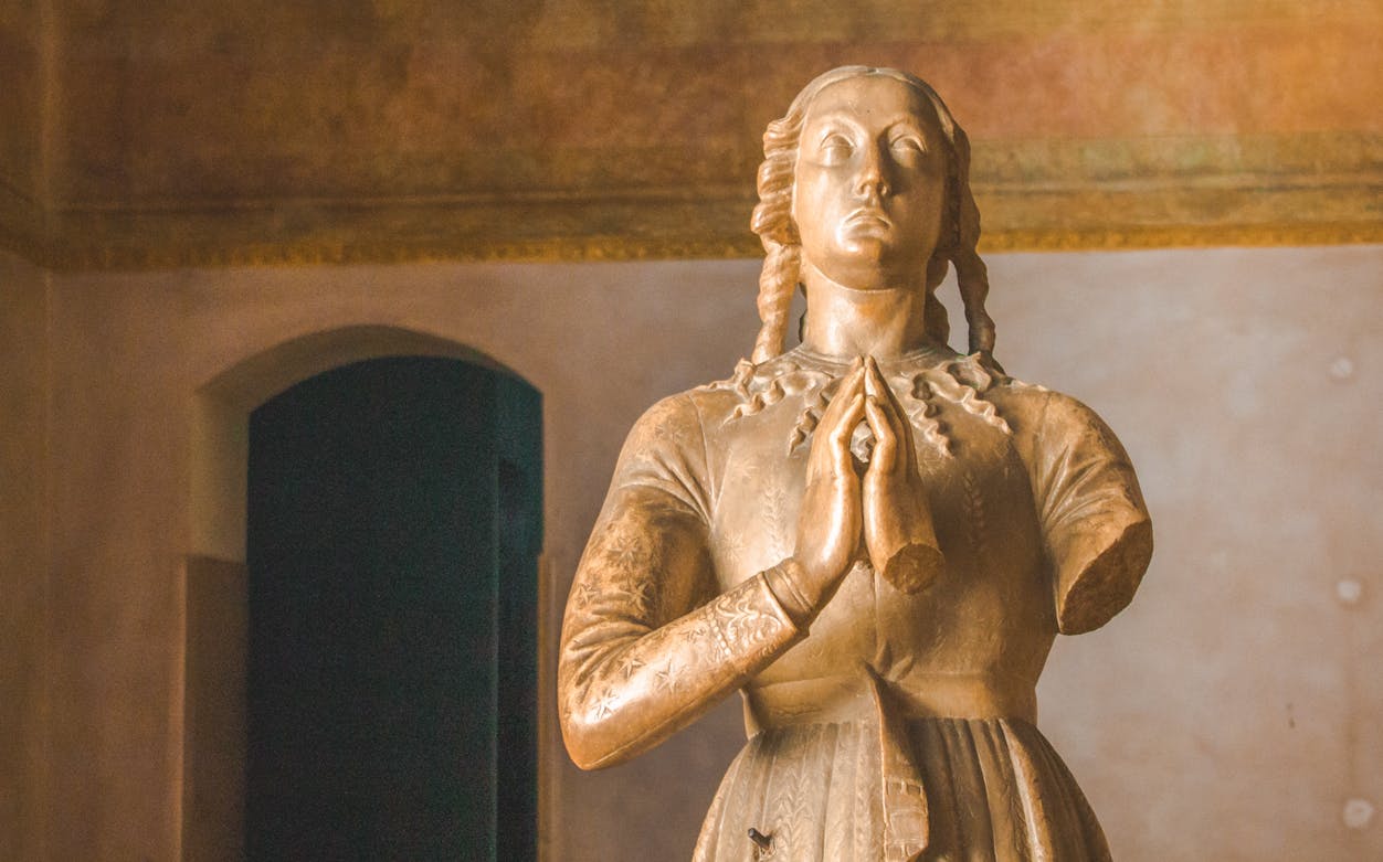 Statue of a praying figure inside Sforza Castle, Milan, featured in self-guided audio tour.
