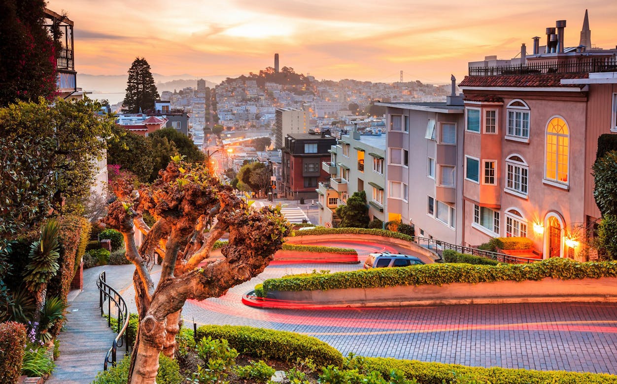 Lombard Street in San Francisco at sunset, featuring winding road and cityscape.