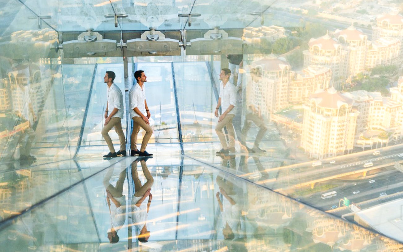 Man walking on glass bridge at Sky View Dubai with cityscape below.