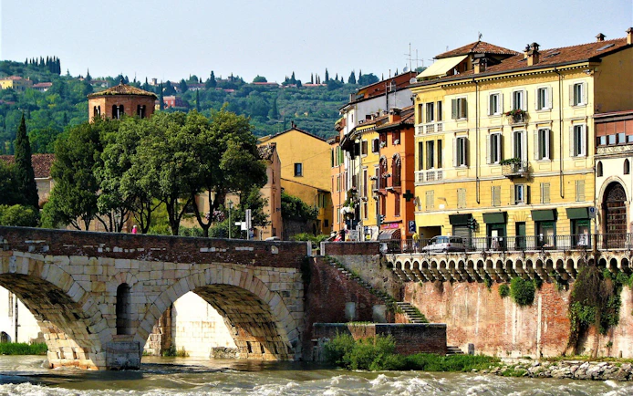 Verona's Ponte Pietra bridge with colorful buildings and lush greenery in the background.