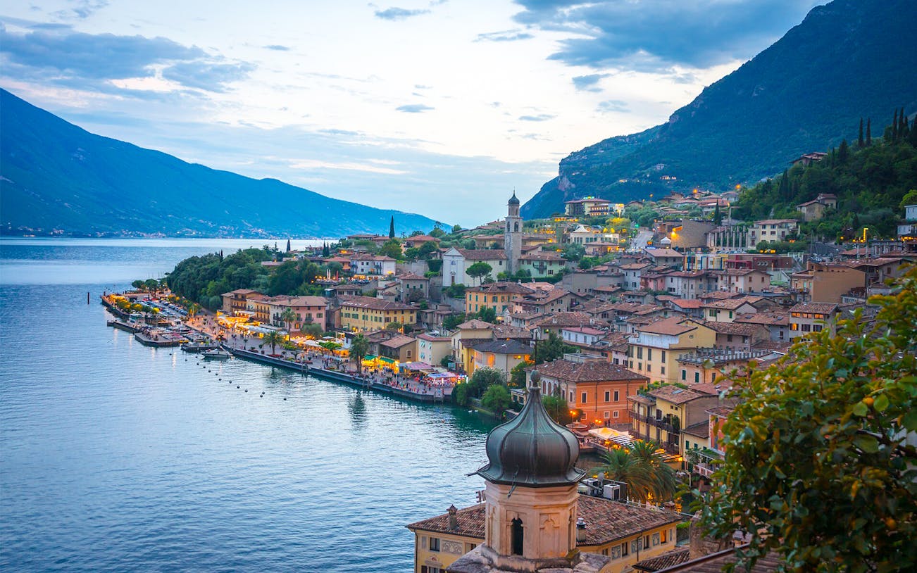Verona and Lake Garda townscape with waterfront and mountains at dusk.