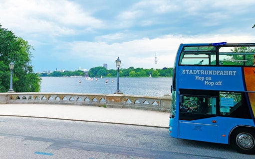 HopOn HopOff bus by a lake with sailboats and city skyline in the background.