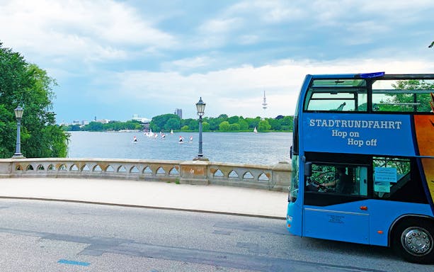 HopOn HopOff bus by a lake with sailboats and city skyline in the background.