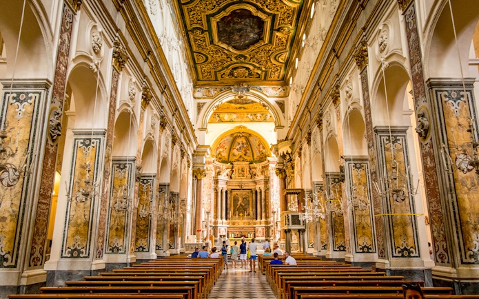 Interior of a historic church in Amalfi with ornate ceiling and visitors exploring.