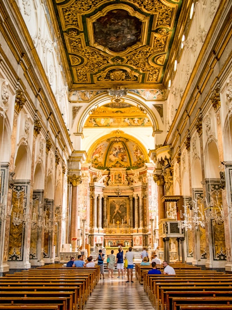Interior of a historic church in Amalfi with ornate ceiling and visitors exploring.