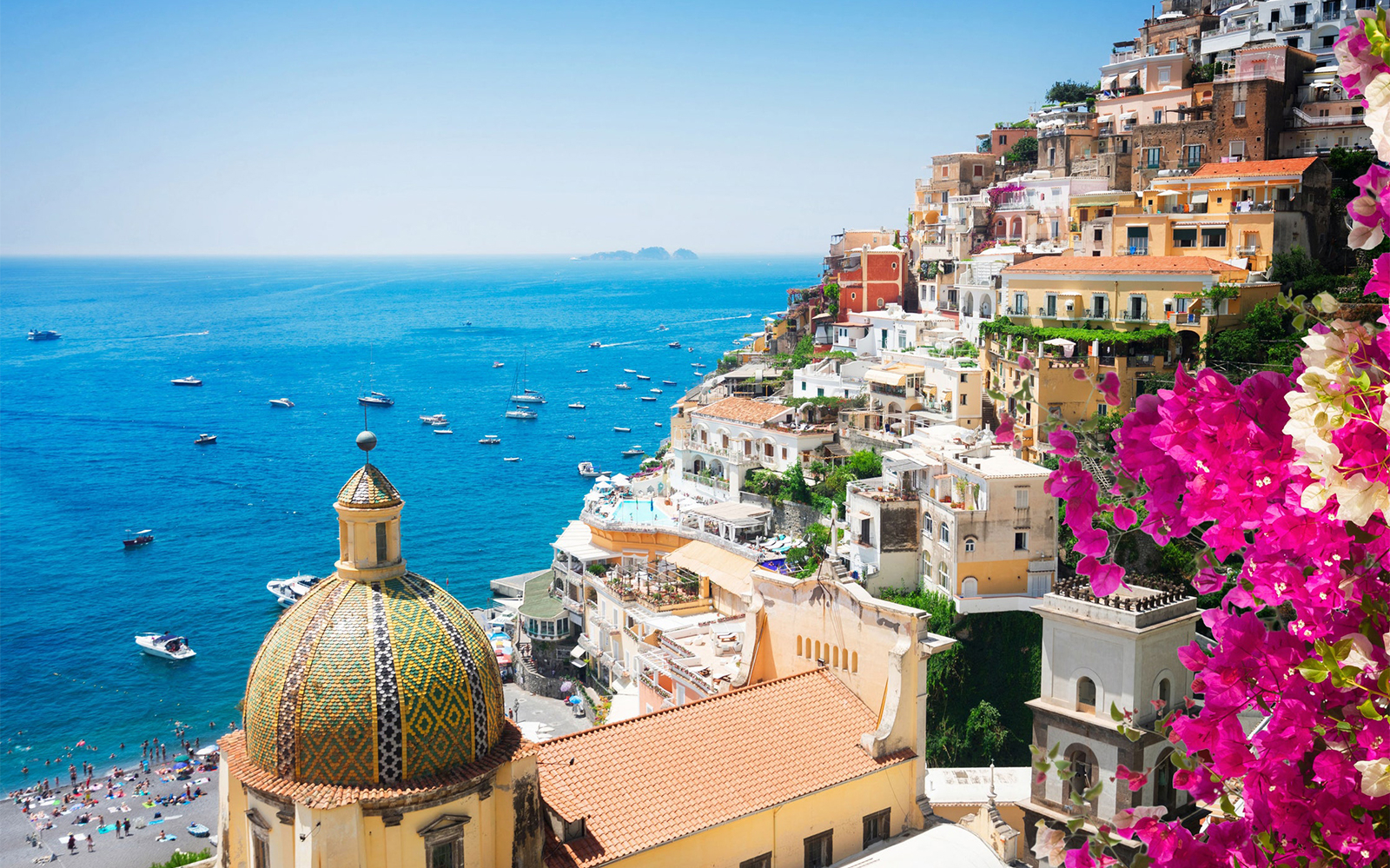Positano coastline with colorful buildings and dome, boats on the Tyrrhenian Sea.