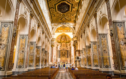 Interior of a historic church in Amalfi with ornate ceiling and visitors exploring.
