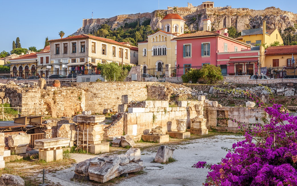 Ancient ruins with colorful buildings and Acropolis of Athens in the background.