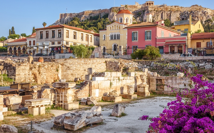 Ancient ruins with colorful buildings and Acropolis of Athens in the background.