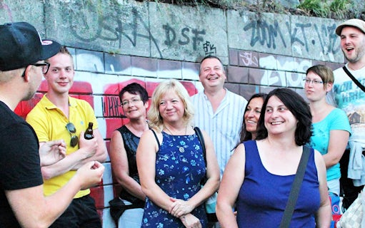 Group of tourists on a guided tour in St. Pauli, Hamburg, standing by graffiti-covered wall.