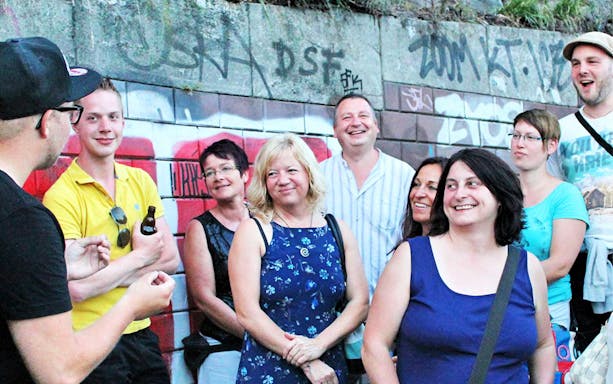 Group of tourists on a guided tour in St. Pauli, Hamburg, standing by graffiti-covered wall.