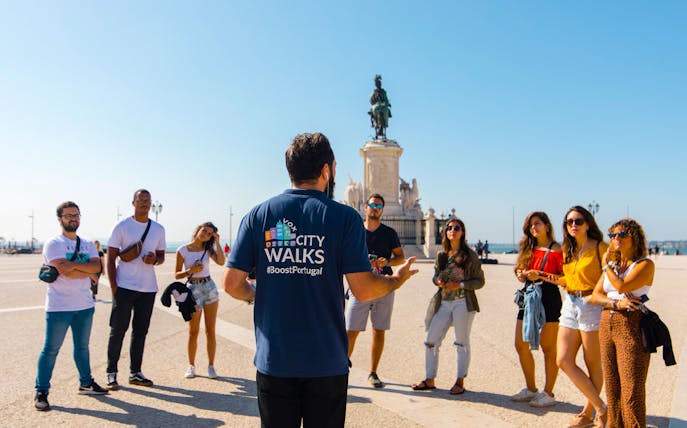 Tour guide leading a group at Praça do Comércio, Lisbon, with equestrian statue in background.