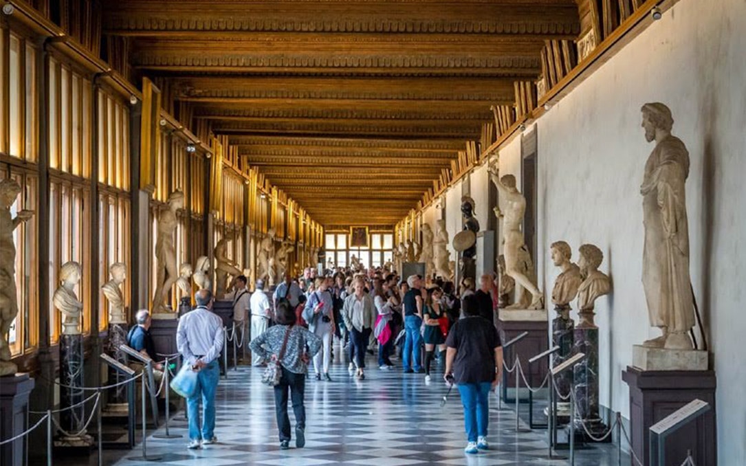 Visitors exploring statue-lined corridor at Uffizi Gallery, Florence, during guided audio tour.