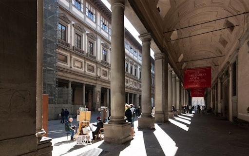 Uffizi Gallery exterior with visitors and street artists in Florence, Italy.