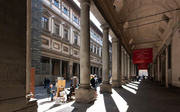 Uffizi Gallery exterior with visitors and street artists in Florence, Italy.