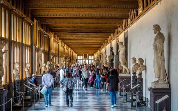 Visitors exploring statue-lined corridor at Uffizi Gallery, Florence.