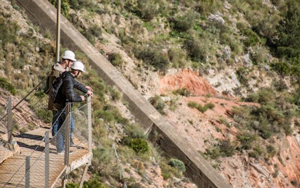 Visitors on a walkway at Caminito del Rey, Málaga, wearing safety helmets.