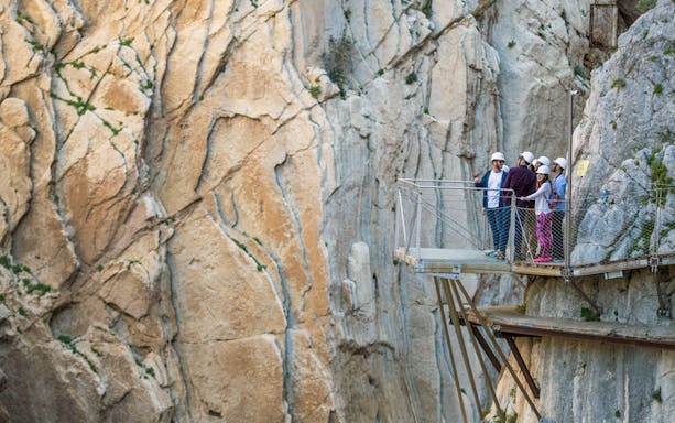 Visitors on a walkway at Caminito del Rey, Málaga, with rocky cliffs in the background.