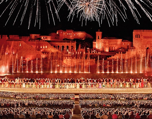 Puy du Fou España entrance at dusk with visitors gathering for El Sueño de Toledo night show, Toledo, Spain.