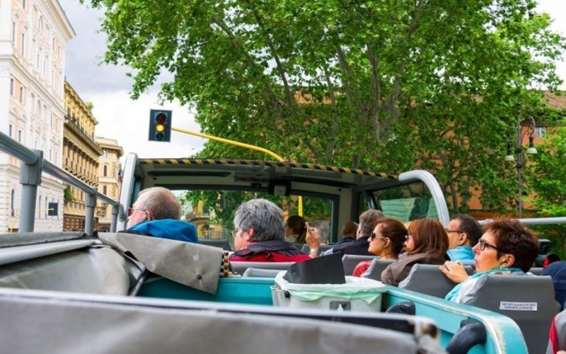 Open-top bus tour in Rome with passengers enjoying city views.