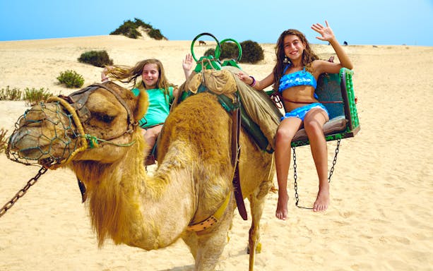 Children riding a camel in Fuerteventura's Oasis Wildlife desert landscape.