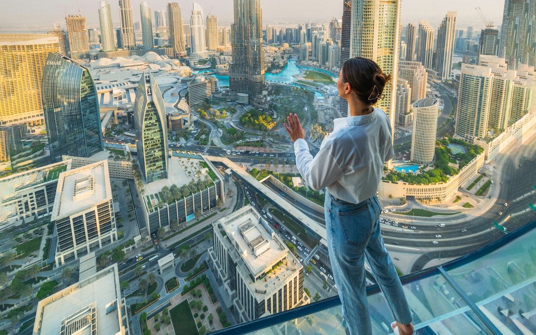 Person standing on glass platform overlooking Dubai skyline during Sky Views Edge Walk Experience.