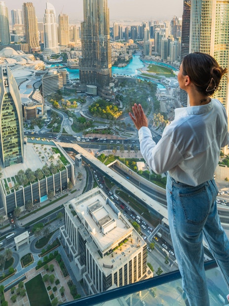 Person standing on glass platform overlooking Dubai skyline during Sky Views Edge Walk Experience.