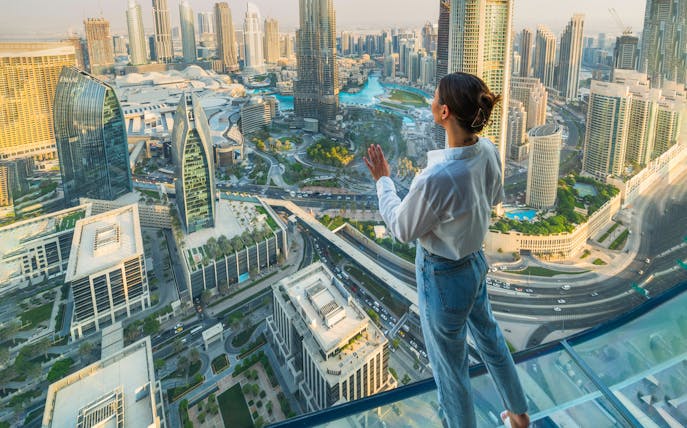Person standing on glass platform overlooking Dubai skyline during Sky Views Edge Walk Experience.