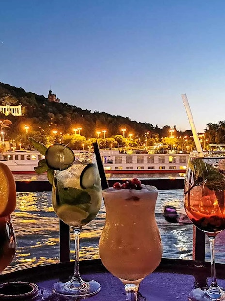 Cocktails on a table with Budapest's illuminated skyline and Danube River at sunset.