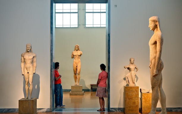 Visitors observing ancient Greek statues at the National Archaeological Museum.