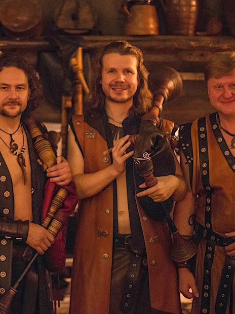 Musicians in medieval attire holding bagpipes at a themed dinner event.